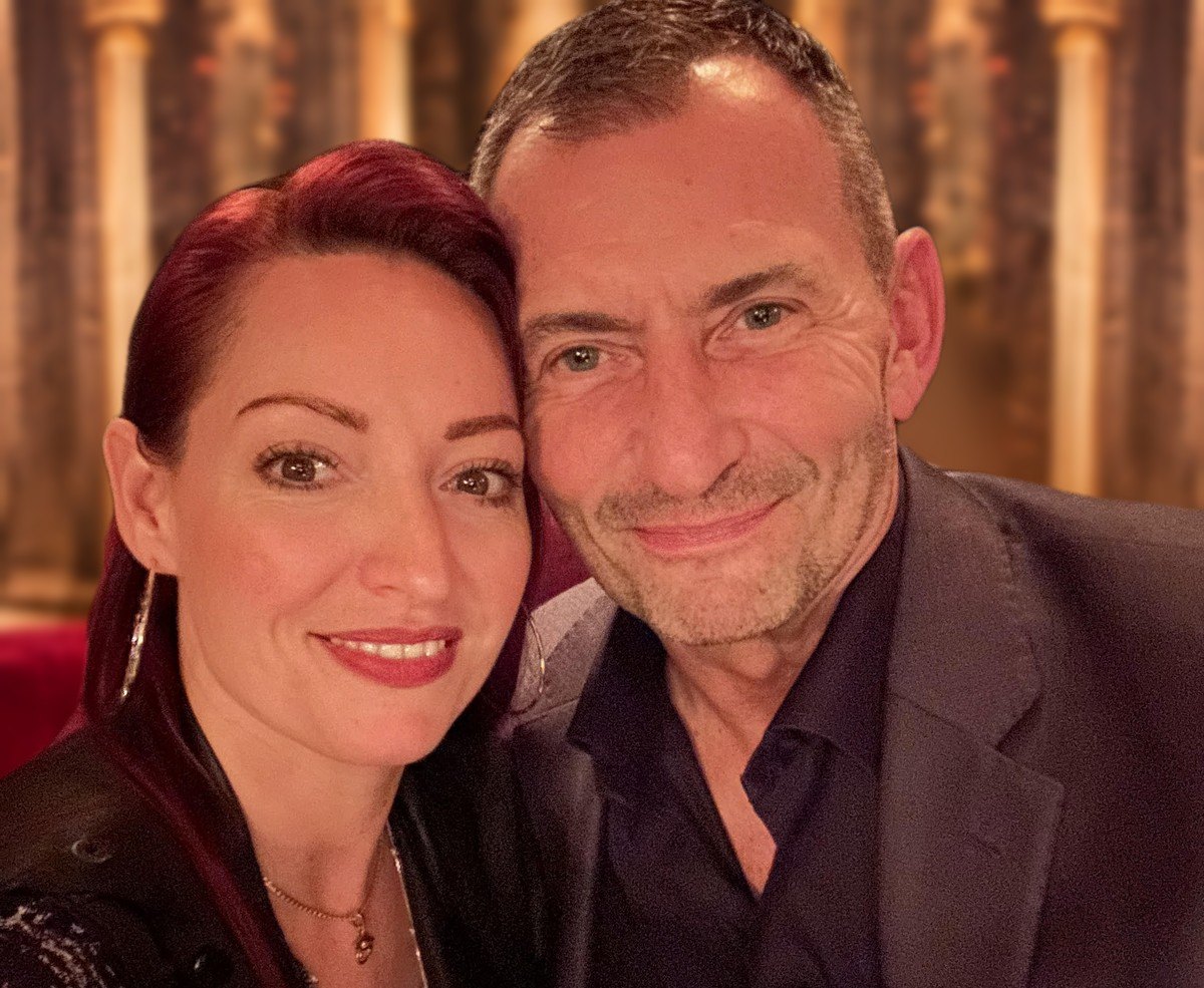 Jaklyn Evaa Royal and Christoph Roman Streubert, founders of Living a Noble Life, cheek to cheek in a candlelit room with gilded columns and red velvet